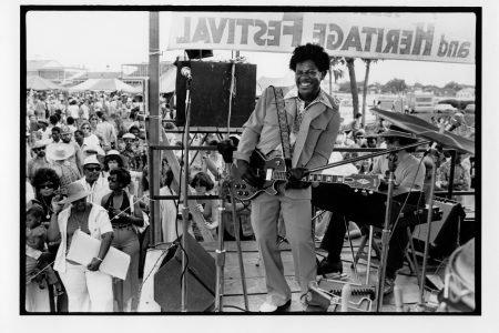 View of Earl King (1934-2003) performing at the 1975 New Orleans Jazz and Heritage Festival. He is seen playing guitar on an outdoor stage while an unidentified musician sits on a keyboard behind him. Earl King performed on Saturday, April 26 at 2 p.m. on Stage 1.